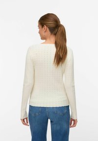 Langarm, crème kleurige geribbelde trui met een fijn patroon en een ronde halslijn, gecombineerd met blauwe high-waisted jeans.