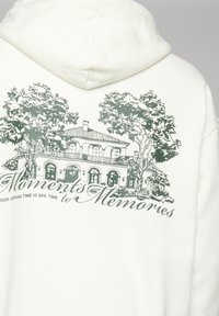 Dos du sweat à capuche avec une esquisse verte d'une grande maison entourée d'arbres et le texte "Des moments aux souvenirs."