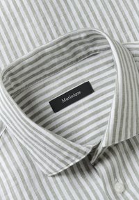 Chemise à rayures verticales vertes et blanches avec un col et une étiquette noire portant l'inscription "Matinique" à l'intérieur du col.