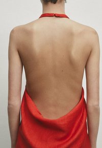 Robe rouge à col licou avec une large découpe dans le dos, confectionnée dans un tissu léger et texturé, mettant en valeur des lignes fluides et un design minimaliste.
