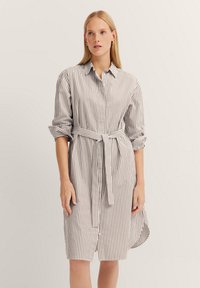 Gestreiftes Hemdkleid aus leichtem Material, mit Kragen, Knopfleiste, gerollten Ärmeln und einem Stoffgürtel für eine maßgeschneiderte Passform. Neutrale Farbtöne.