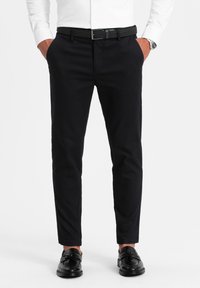 Pantaloni neri su misura realizzati in tessuto intrecciato, caratterizzati da una vestibilità slim, davanti piatto, tasche laterali e abbinati a scarpe nere e a una cintura.
