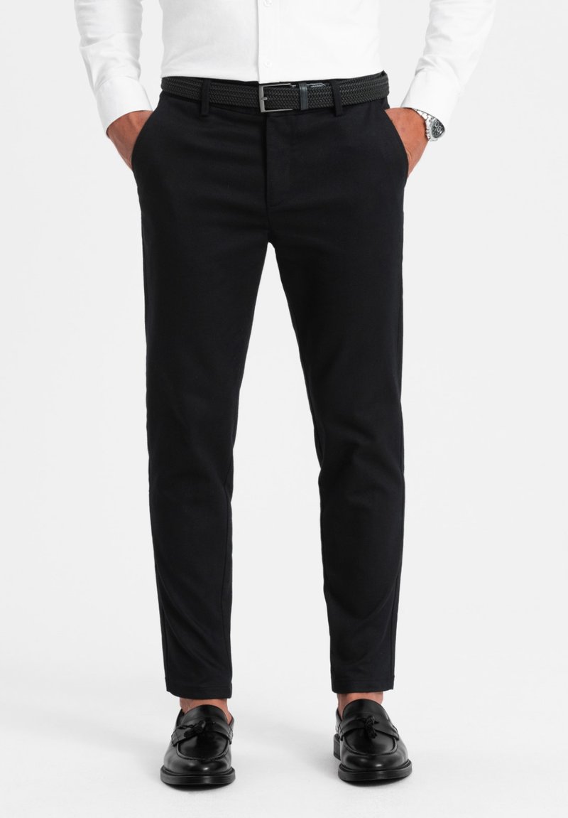 Pantaloni neri su misura realizzati in tessuto intrecciato, caratterizzati da una vestibilità slim, davanti piatto, tasche laterali e abbinati a scarpe nere e a una cintura.