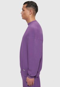 Lila Sweatshirt aus weichem Material, mit Rundhalsausschnitt, überschnittenen Schultern und gerippten Bündchen. Minimale Markenkennzeichnung am Saum.