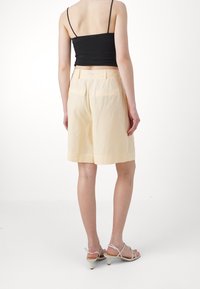 Shorts giallo chiaro realizzati in tessuto morbido, con un taglio dritto, due tasche posteriori e una vita a media altezza.