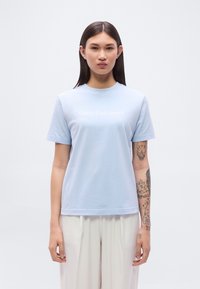 Ανοιχτό μπλε βαμβακερό μπλουζάκι με στρογγυλή λαιμόκοψη και κοντά μανίκια, με το κείμενο «Calvin Klein Jeans» τυπωμένο σε λευκό στην μπροστινή όψη.