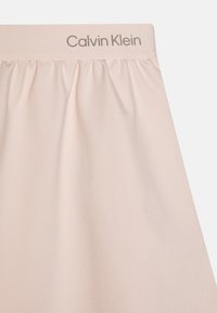Calvin Klein light pink skirt with gathered waist, soft fabric texture, and subtle branding at the waistband. Simple, minimalist design.