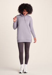 Light purple sweatshirt tunic with a high collar, long sleeves, and side zippers, paired with dark leggings and white sneakers.