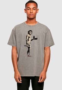 Graues oversize T-Shirt mit einem Grafikdesign eines Höhlenmenschen, der Essen und ein Getränk hält, mit sichtbaren Nähten und kurzen Ärmeln.