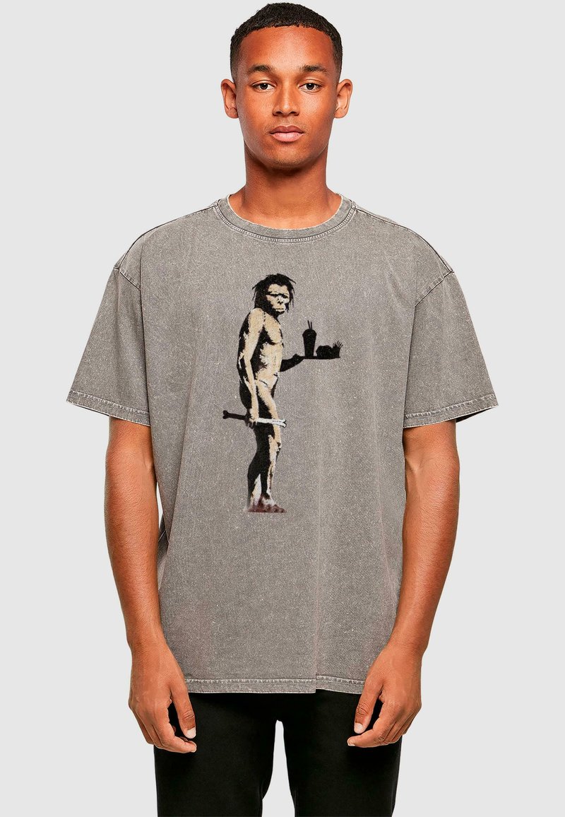 Graues oversize T-Shirt mit einem Grafikdesign eines Höhlenmenschen, der Essen und ein Getränk hält, mit sichtbaren Nähten und kurzen Ärmeln.