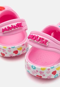 Roosa libistatavate puugidega, millel on Minnie Mouse'i bränding, mustriga valge tallaga, kus on südamed ja lilled, valmistatud kergetest materjalidest.