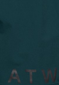 Ciemnoturkusowa tkanina z dużymi czarnymi literami "A", "T" i "W" nadrukowanymi w pobliżu dolnej krawędzi.