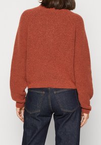 Rotskleurige gebreide trui met een geribbelde textuur, raglanmouwen en een cropped ontwerp, gecombineerd met donkere spijkerbroek.