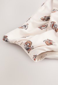 Tissu blanc avec petits motifs floraux orange et bleu, avec des bords élastiqués froncés.