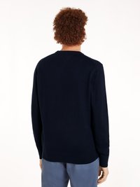 Pull en bleu marine en tissu tricoté doux, avec un col rond et des poignets côtelés, texture lisse et silhouette ajustée.
