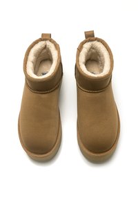 Botas tobilleras de ante marrón con forro de piel sintética, punta redonda y detalles de costura. Pestañas en la parte posterior para facilitar su puesta.