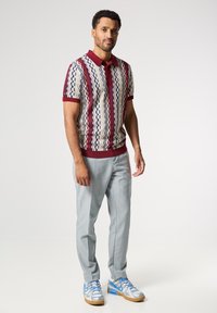 Polo de manga corta con un patrón a rayas en crema, burdeos y azul; combinado con pantalones grises claros y zapatillas deportivas azules.