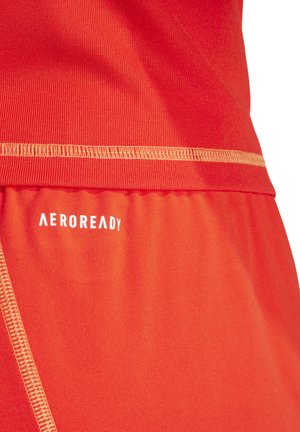 Roter Sportstoff mit glatter Textur und kontrastierender gelber Naht. Das "AEROREADY"-Logo in Weiß ist im unteren Bereich aufgedruckt.