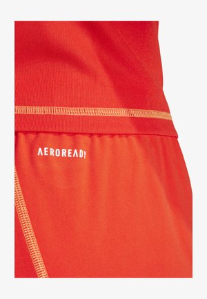 Roter Sportstoff mit glatter Textur und kontrastierender gelber Naht. Das "AEROREADY"-Logo in Weiß ist im unteren Bereich aufgedruckt.