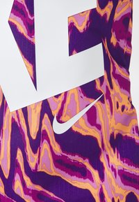 Nike sportinė apranga su banguota marmuro raštu purpurinėje, rožinėje ir oranžinėje spalvose, dideli baltos spalvos logotipai ant tekstūruoto audinio.