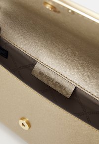 Bolso de mano dorado con un exterior texturizado, que presenta un cierre a presión y un bolsillo interior etiquetado con "MICHAEL KORS". Forrado en tela.