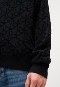 Mustat neulotut neuletakit, joissa on kohokuvioitu timanttikuvio, ohuet resorit ja sileä lankakudos. Yhdistettynä sinisiin farkkuihin.