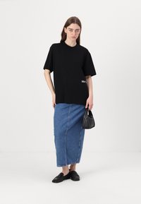 Svart oversized t-skjorte med korte ermer, kombinert med et langt denimskjørt. En svart håndveske og svarte slip-on sko fullfører antrekket.