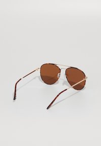 Ochelari de soare cu nuanță cafenie, rama din material scoică, accente din metal auriu și brațe subțiri, având un design elegant, rotund.