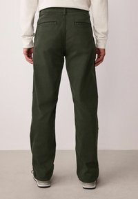 Khakigrüne Hose mit geradem Schnitt, zwei Gesäßtaschen und einer glatten Textur. Tragen Sie dazu ein hellfarbenes Langarmhemd.