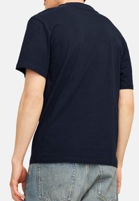 Navy blue short-sleeve t-shirt with a round neckline and soft texture, viewed from the back. Worn with light blue denim jeans.