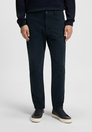 Dunkelblaue Chinos mit glatter Textur, Slim Fit, ausgestattet mit einem Knopfverschluss und Fronttaschen, kombiniert mit schwarzen Sneakers.