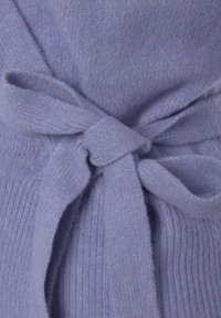 Lichtpaarse wolwrap met een gestructureerde afwerking, voorzien van een gestrikt riemdetail dat de zachtheid en warmte benadrukt.