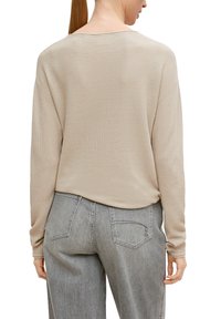 Beige Strickpullover mit lockerer Passform, weitem Ausschnitt und strukturiertem Muster, kombiniert mit hochgeschnittenen, hellgrauen Jeans.