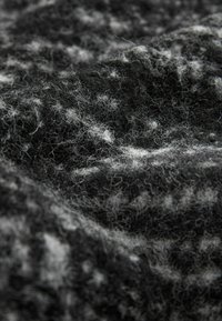Gros plan sur un tissu en laine texturé noir et gris avec des fibres visibles et un motif de surface doux et duveteux.
