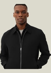 Giacca nera con zip, colletto, tasche laterali e logo discreto. Tessuto morbido con una vestibilità strutturata e design minimalista.