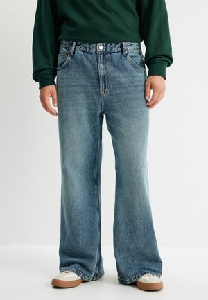 Helle blaue, weite Denim-Jeans. Verfügt über ein Five-Pocket-Design mit einer Vorderknopfverschluss und subtilen Verblassungen. Getragen mit neutralen Sneakers.