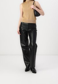 Beżowy top bez rękawów z wysokim kołnierzem, zestawiony z czarnymi, skórzanymi spodniami o wysokim stanie i czarną torebką. Gładkie tekstury i dopasowany krój.