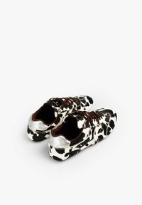 Zapatillas con estampado de vaca que presentan un exterior texturizado de pelo sintético, detalles plateados en el talón y cordones marrones. Punta redondeada y diseño de corte bajo.