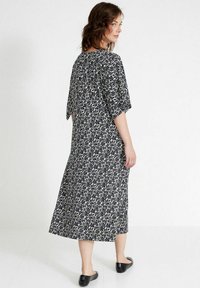 Schwarzes und weißes Blumenmuster-Kleid mit lockerer Passform, mittel-langen Ärmeln und fließender Silhouette, kombiniert mit schwarzen flachen Schuhen.