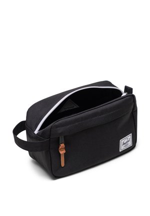 Musta suorakulmainen toilettikassi, joka on valmistettu kestävästä kankaasta. Kassissa on valkoinen vetoketju, nahkavedin ja etupuolella logo-patch.