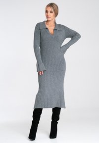 Długa, prążkowana sukienka w jasnoszarym kolorze z dekoltem w kształcie litery V i kołnierzykiem. Dopasowany krój z rozszerzanymi rękawami, zestawiona z czarnymi botkami do kolan.