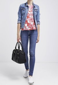 Giacca di jeans, top floreale a maniche corte in rosso e bianco, jeans skinny blu, borsa nera e sneakers bianche. Design e colori semplici.