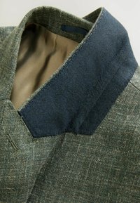 Textūruotas žalias audinio apykaklė su tamsiai mėlynu akcentu, turinti lygų vidinį pamušalą. Siuvinėjimas išilgai kraštų.