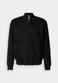 Black suede bomber jacket featuring a full zip closure, ribbed cuffs and hem, with a minimalist logo detail on the chest.