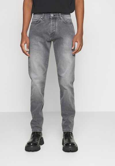 Calças de ganga cinzentas com um corte slim, apresentando um efeito de desbotado, design de cinco bolsos e costura em contraste. Combinadas com botas pretas robustas.