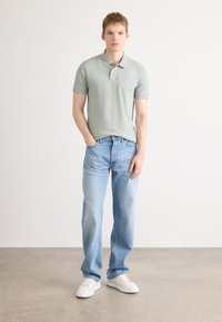 Lys grønn bomullspolo med krage og liten logo, sammen med lyseblå rette jeans og hvite sneakers.