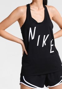 Czarny bezrękawnik z dużym białym logo "NIKE", wykonany z lekkiego materiału, w zestawie z czarnymi szortami sportowymi z białymi wykończeniami.