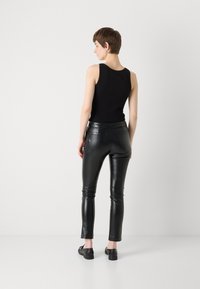 Musta hihaton paita yhdistettynä tiukkoihin mustiinNahkahousuihin. Tasainen pinta, slim fit, näkyvillä takataskuilla ja nilkkapituisella leikkauksella.