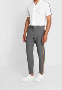 Šedé tailored kalhoty s úzkým střihem, s multicolor pruhy na straně, spárované s jednoduchou bílou košilí s krátkým rukávem a bílými teniskami.