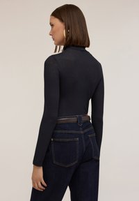 Top lung cu maneci lungi, de culoare neagră, cu guler înalt, având o textură raiată. Asortat cu blugi inchisi la culoare și o curea maro. Design simplu și ajustat.